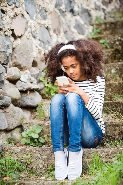 Akıllı telefon ve kulaklık ile güzel Afro-Amerikan kız. — Stok fotoğraf