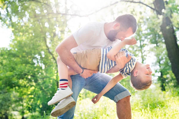 Junger Vater mit kleinem Sohn im grünen Wald, sonniger Tag. — Stockfoto