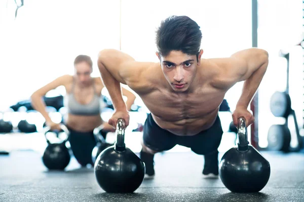 Jonge paar passen in de sportschool doet push ups op kettlebells — Stockfoto