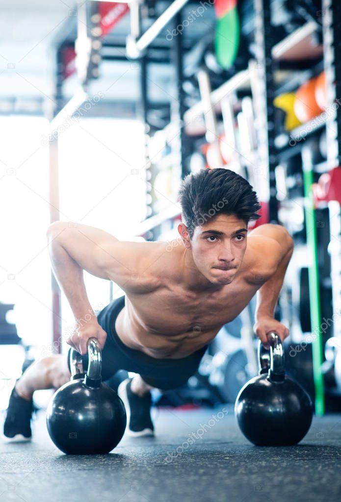 Young fit hispanic man in gym doing push ups on kettlebells