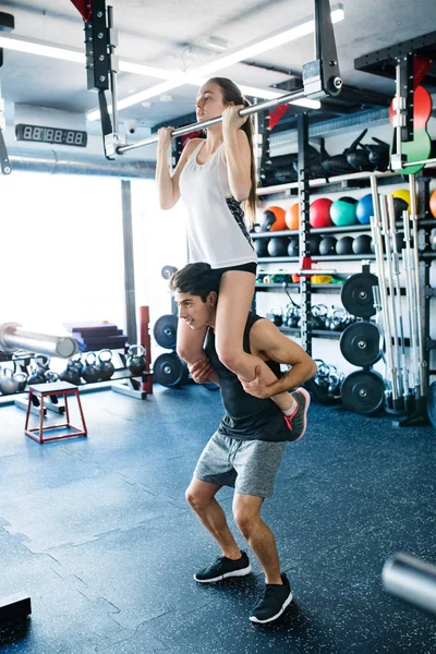 女人在健身房做拉 ups，男人给她背. — 图库照片