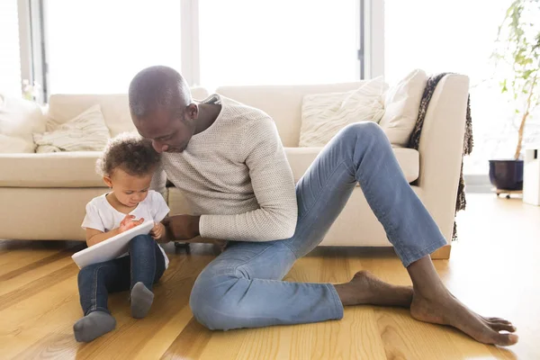 Padre afro-americano con su pequeña hija en casa sosteniendo la tableta . —  Fotos de Stock