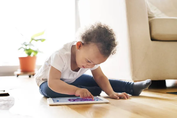 Pequena menina de raça mista em casa jogando jogo no tablet . — Fotografia de Stock