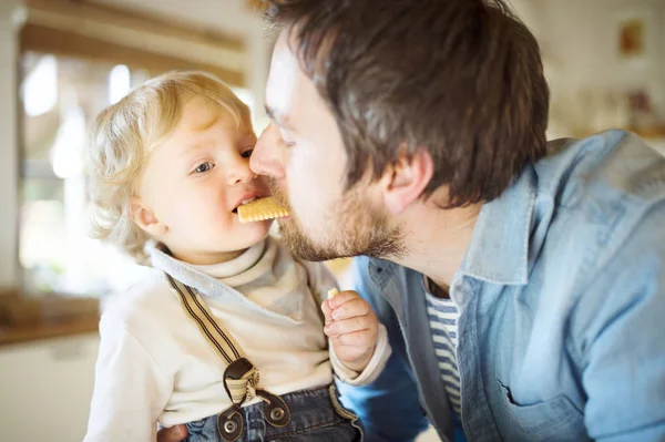 Молодой отец дома со своим маленьким сыном, который ест печенье вместе . — стоковое фото