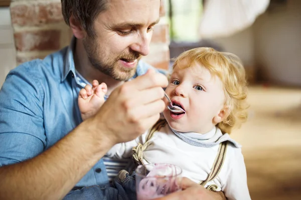 Jovem pai em casa alimentando seu filho com iogurte . — Fotografia de Stock
