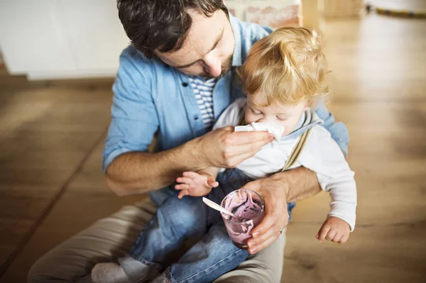 Padre joven en casa alimentando a su pequeño hijo con yogur . —  Fotos de Stock