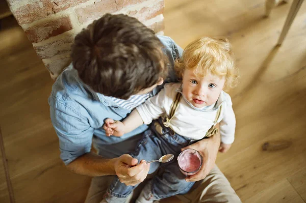 Padre joven en casa alimentando a su pequeño hijo con yogur . — Foto de Stock