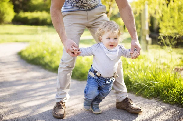 K nepoznání otec drží za ruce jeho syna podniká první kroky — Stock fotografie