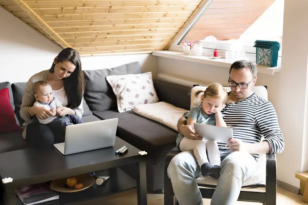 Jovens pais com crianças pequenas e gadgets em casa . — Fotografia de Stock