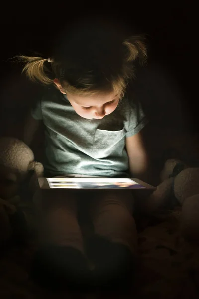 Niña en casa por la noche viendo algo en la tableta . — Foto de Stock