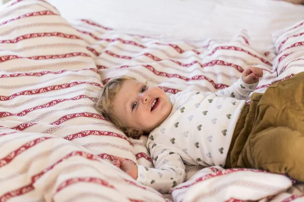 Ładny mały chłopiec w domu, leżąc na łóżku uśmiechając się. — Zdjęcie stockowe