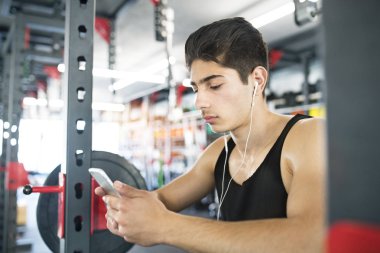 Dinlenme, akıllı telefon tutarak, müzik dinleme spor salonunda İspanyol adam