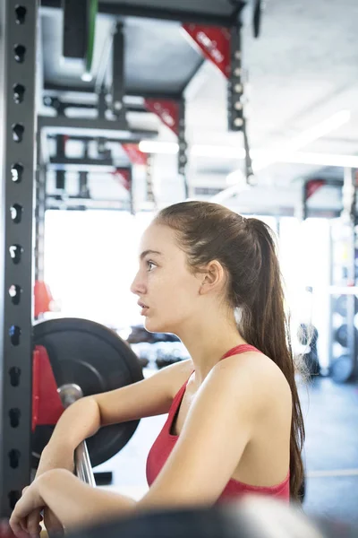Молода жінка в спортзалі стоїть біля важкого барбелла — стокове фото