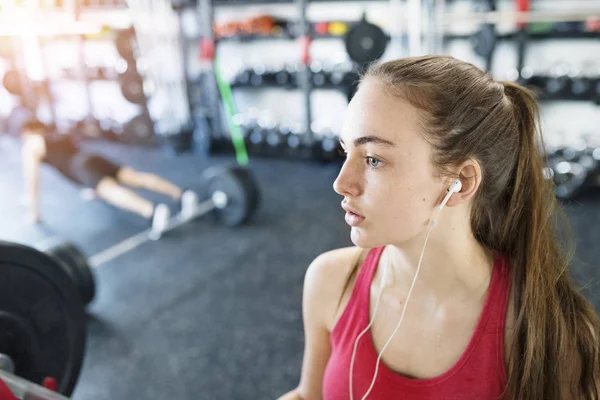 年轻女子在健身房，在她的耳朵，听音乐的耳机 — 图库照片