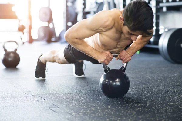 Jonge Spaanse man past in sportschool doen push ups op kettlebell. — Stockfoto