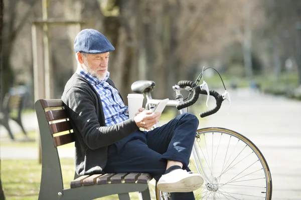 Uomo anziano in panchina con bicicletta e smartphone, sms . — Foto Stock