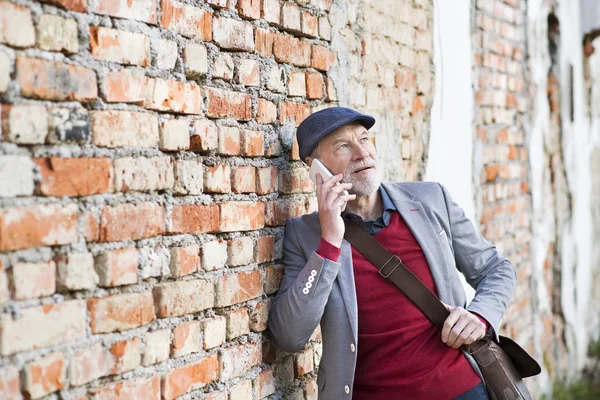 Homme âgé avec smartphone faisant un appel téléphonique contre un mur de briques . — Photo