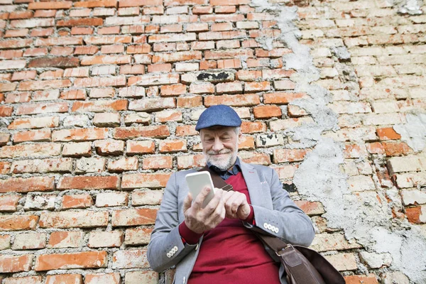 Старший мужчина со смартфоном против кирпичной стены, смс . — стоковое фото