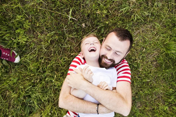 Hipster father and little son lying on green meadow. Summer day. — Stock Photo, Image