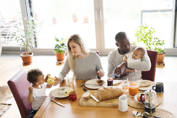 Joven familia interracial con niños pequeños desayunando . —  Fotos de Stock