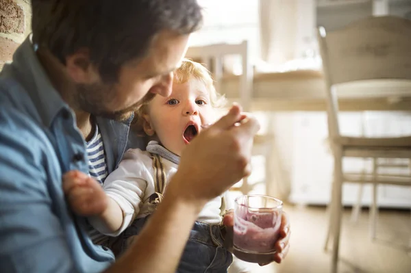 Jovem pai em casa alimentando seu filho com iogurte . — Fotografia de Stock