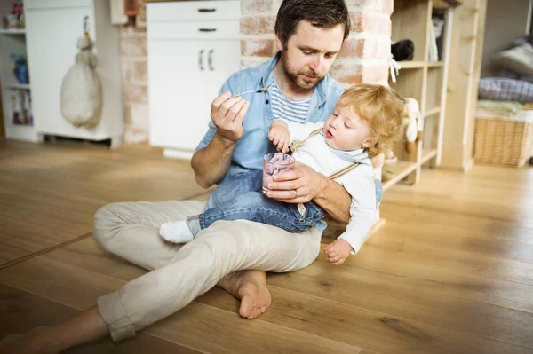 Padre joven en casa alimentando a su pequeño hijo con yogur . — Foto de Stock