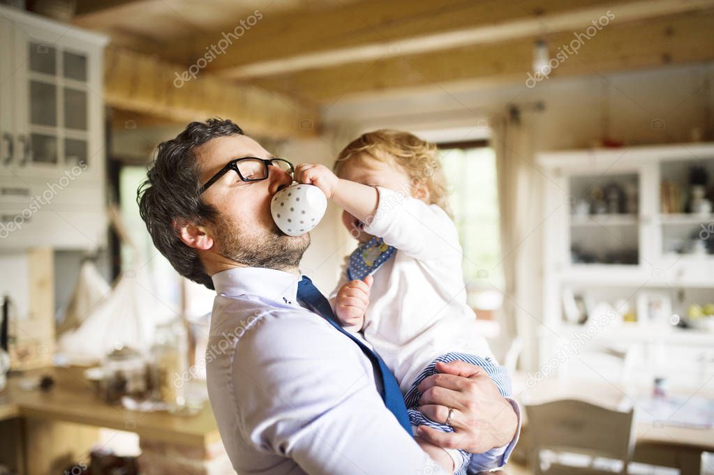 Businessman holding little son in the arms, drinking coffee.