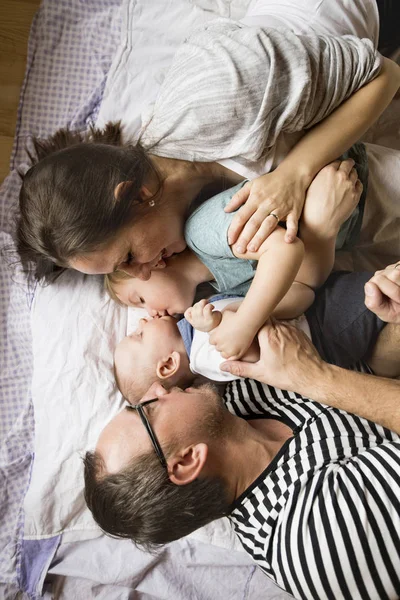 Jonge ouders met kleine kinderen in bed liggen. — Stockfoto