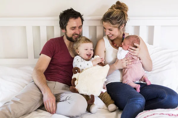 Padres jóvenes en la cama con sus pequeños y lindos hijos — Foto de Stock