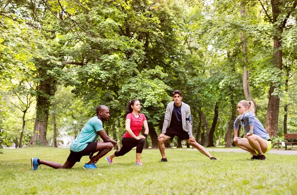 Group of young runners stretching and warming up in park. — Stock Photo, Image