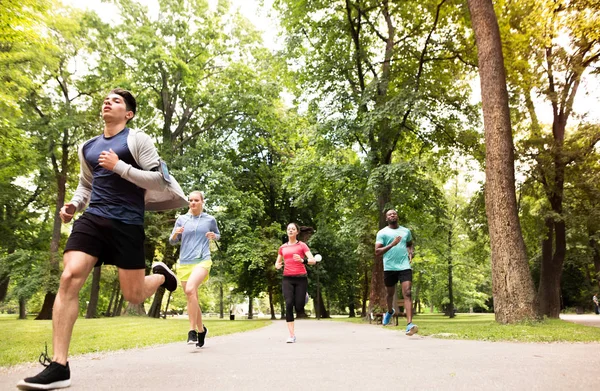 Η ομάδα των νεαρών αθλητών, τρέχουν σε ηλιόλουστο, καταπράσινο πάρκο. — Φωτογραφία Αρχείου