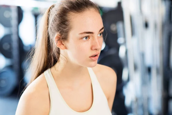Young woman in gym, in white tank top, resting — Stock Photo, Image