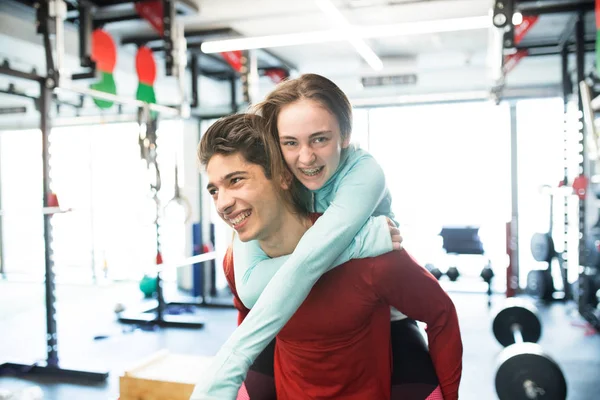 Young man in gym carrying woman on his shoulders. — Stock Photo, Image