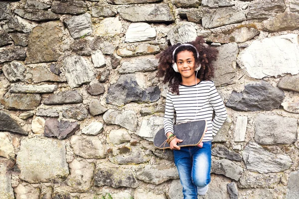 Ragazza afroamericana con skateboard e cuffie . — Foto Stock