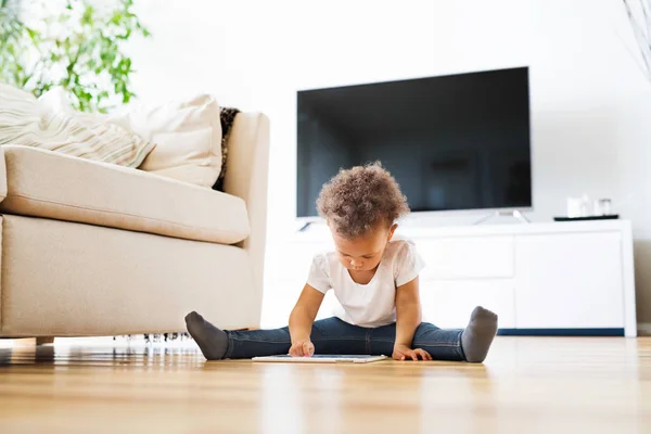 Pequeña chica de raza mixta en casa jugando juego en la tableta . — Foto de Stock