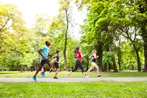 Grupo de jovens atletas correndo no parque ensolarado verde . — Fotografia de Stock