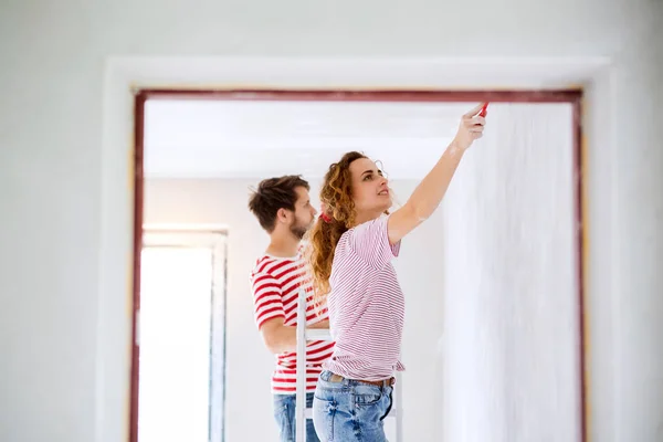 Pareja joven pintando paredes en su nueva casa . — Foto de Stock