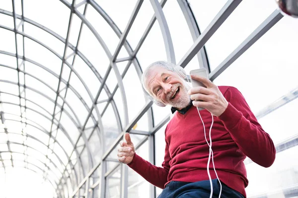 Senior man with smartphone and headphones in passage. — Stock Photo, Image