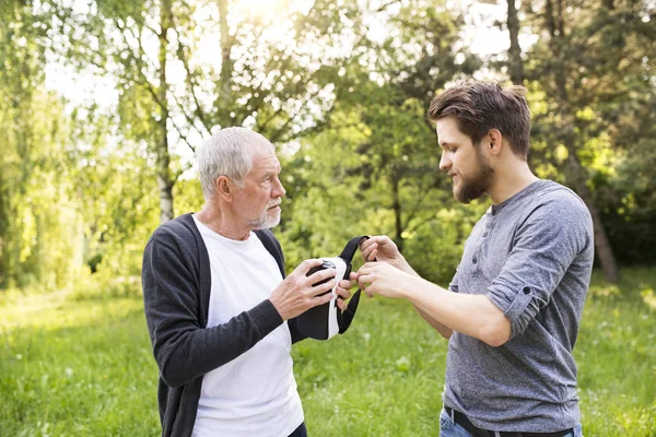 Giovane uomo e suo padre anziano con occhiali VR all'aperto . — Foto Stock