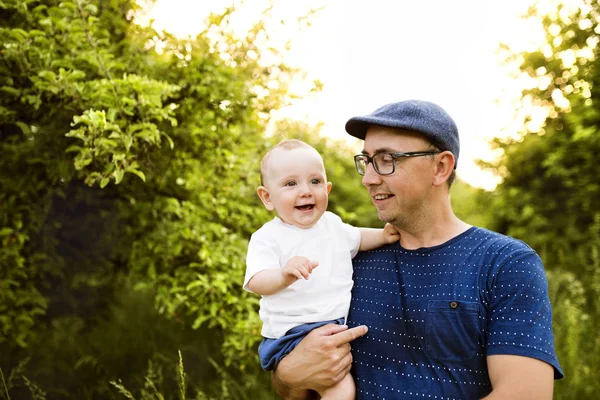 Unga far i naturen håller baby son i armarna. — Stockfoto