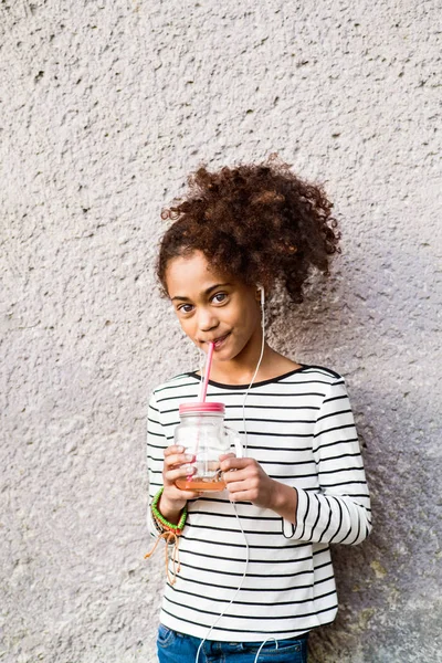 Bella ragazza afro-americana che beve succo, ascoltando musica . — Foto Stock