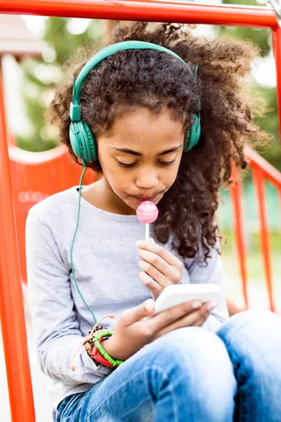 Africano menina americana no parque infantil com mensagens de texto telefone inteligente . — Fotografia de Stock