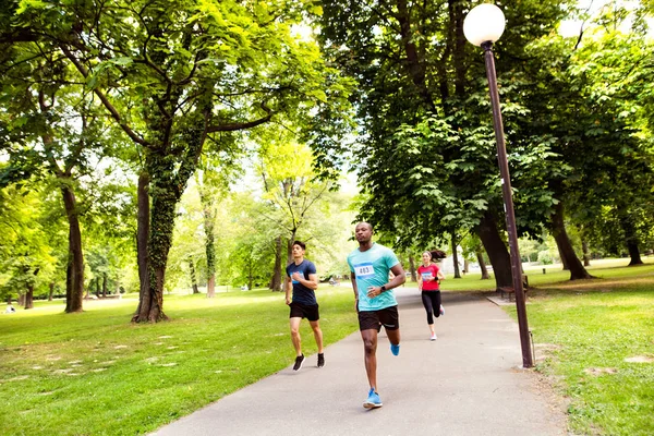 Grupo de jovens atletas correndo no parque ensolarado verde . — Fotografia de Stock