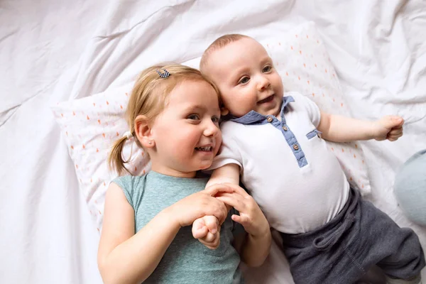 Nettes kleines Mädchen mit ihrem kleinen Bruder auf dem Bett liegend. — Stockfoto