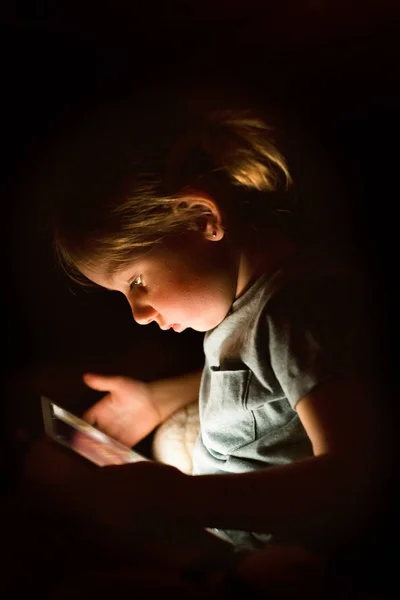 Niña en casa por la noche viendo algo en la tableta . — Foto de Stock