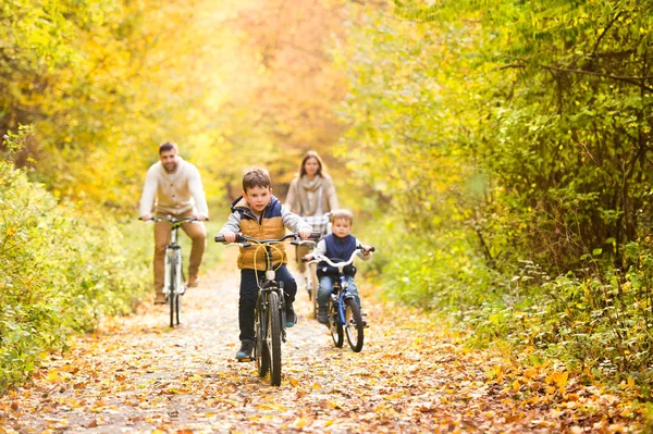 Familia joven en ropa de abrigo en bicicleta en el parque de otoño —  Fotos de Stock