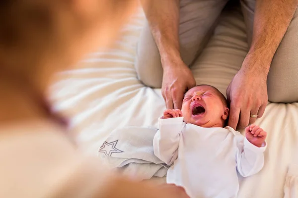 Padres irreconocibles en casa vistiendo a su bebé en la cama . — Foto de Stock