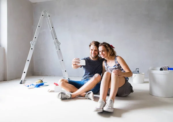 自宅カップルがスマート フォンで selfie を取っての壁を塗る. — ストック写真