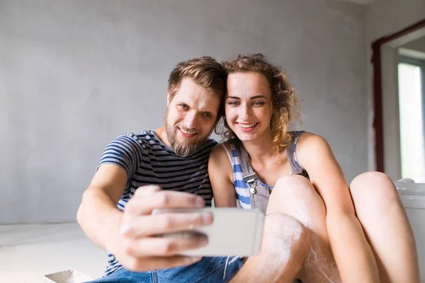 Casal em paredes de pintura em casa, tirando selfie com smartphone . — Fotografia de Stock