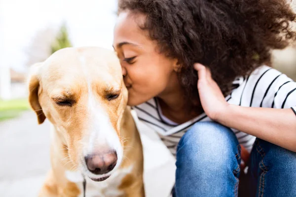 Meisje van de African american buiten met haar hond, zoenen hem. — Stockfoto